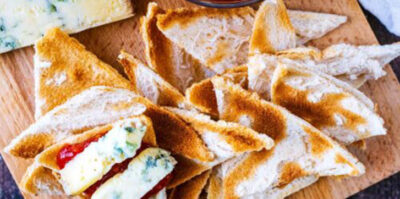 Une planche de service avec des triangles de toasts, du fromage bleu et un bol de chutney.